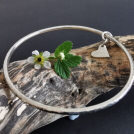 sterling silver bangle with a solid heart charm on driftwood.